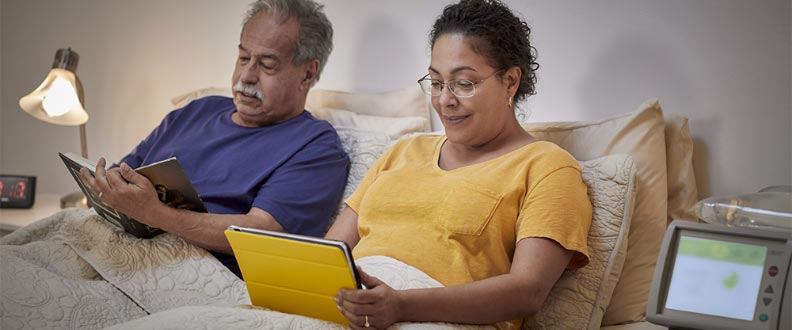 a man and a woman in bed reading with a home dialysis machine